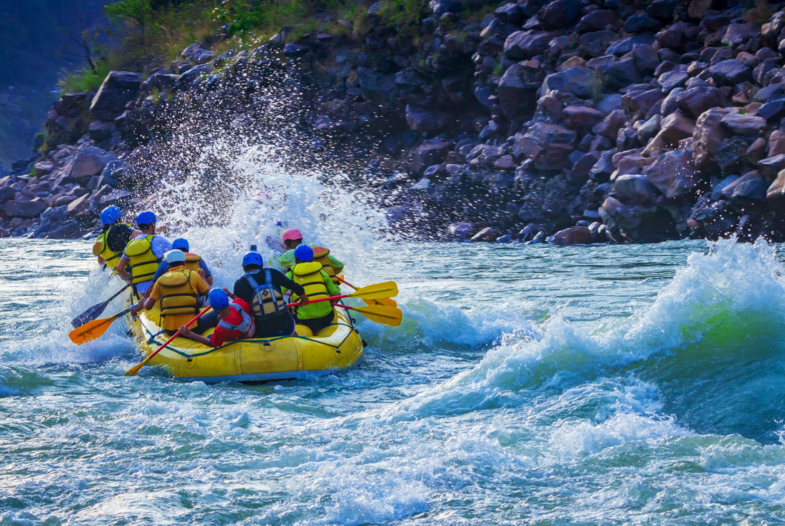 Group in helmets and life jackets white-water rafting in a yellow raft on a river, splashing through rapids near rocky terrain, vibrant scene.