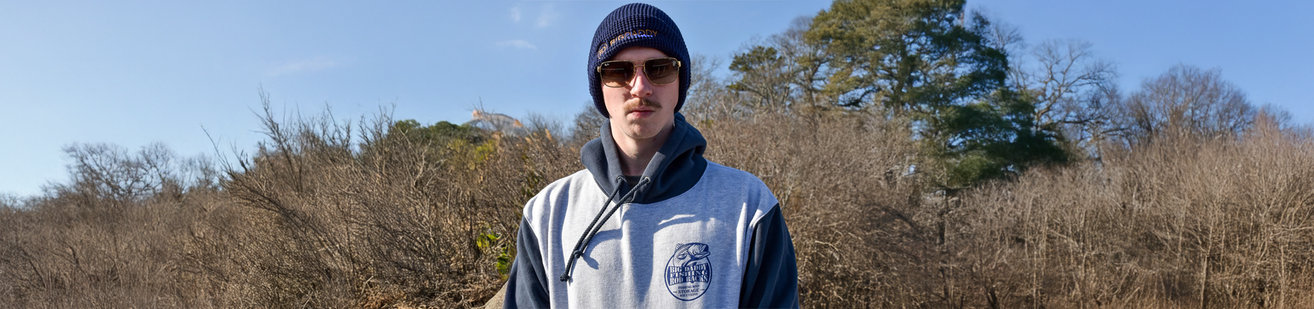 A man standing in front of a wooded area wearing a Big Daddy Life Hoodie and Beanie